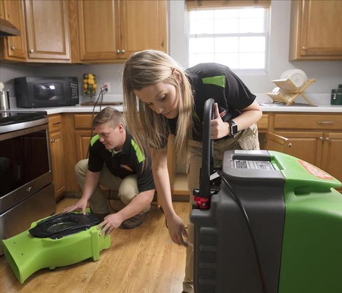 Technicians setting up equipment in a kitchen with water damage.